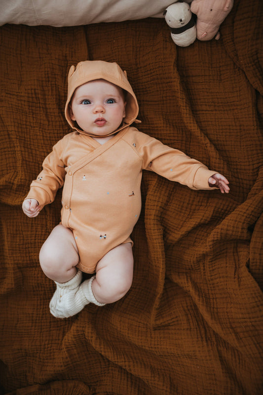 Beige baby onesie with small patterns on a light gray background