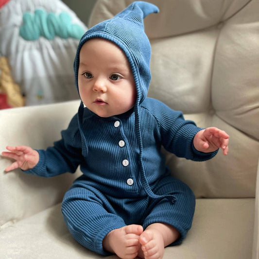 Baby wearing a blue knitted outfit sitting on a beige couch.