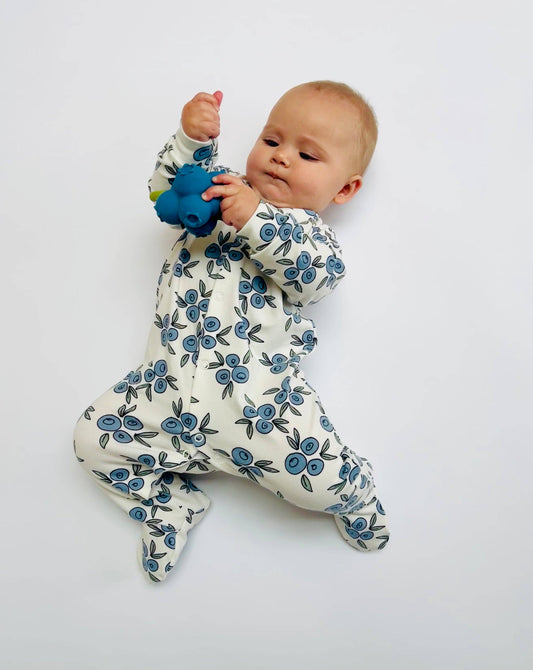 Baby wearing a floral sleepsuit holding a blue toy on a light gray background