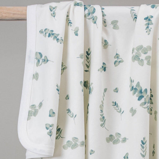 Newborn baby wrapped in a eucalyptus-patterned swaddle with a visible brand label on a soft surface.