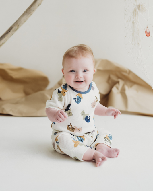Baby wearing a romper with animal prints sitting on a white surface.