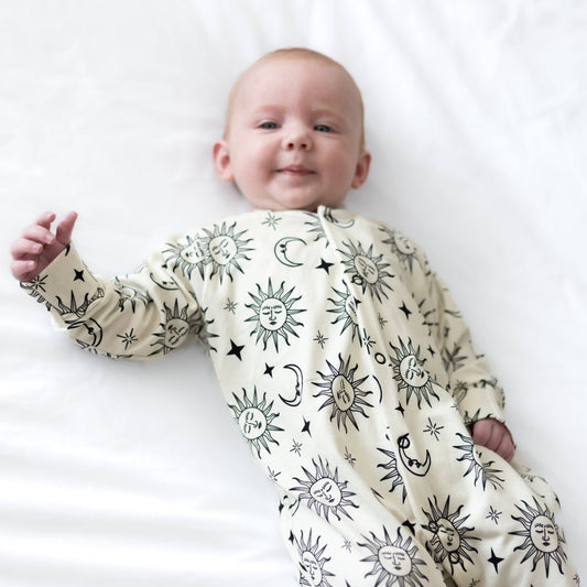 Baby wearing a white sleepsuit with celestial pattern on a white background