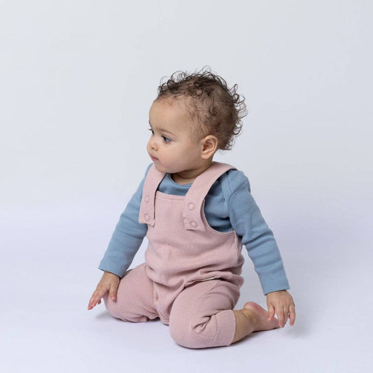 Baby wearing pink dungaree and a blue shirt on a white background