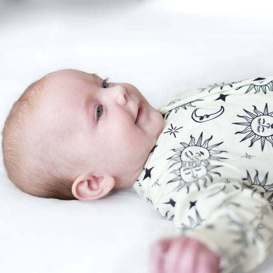 Baby wearing a white sleepsuit with celestial pattern on a white background