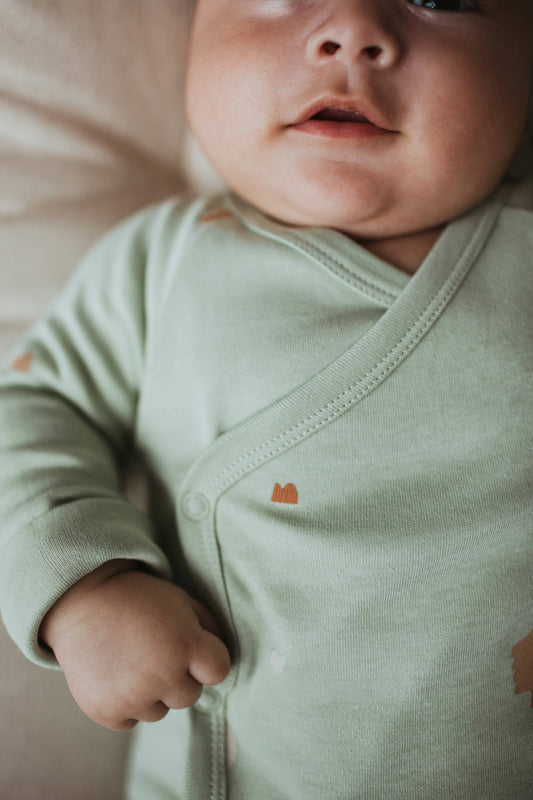 Mint green baby onesie with tree designs on a beige background