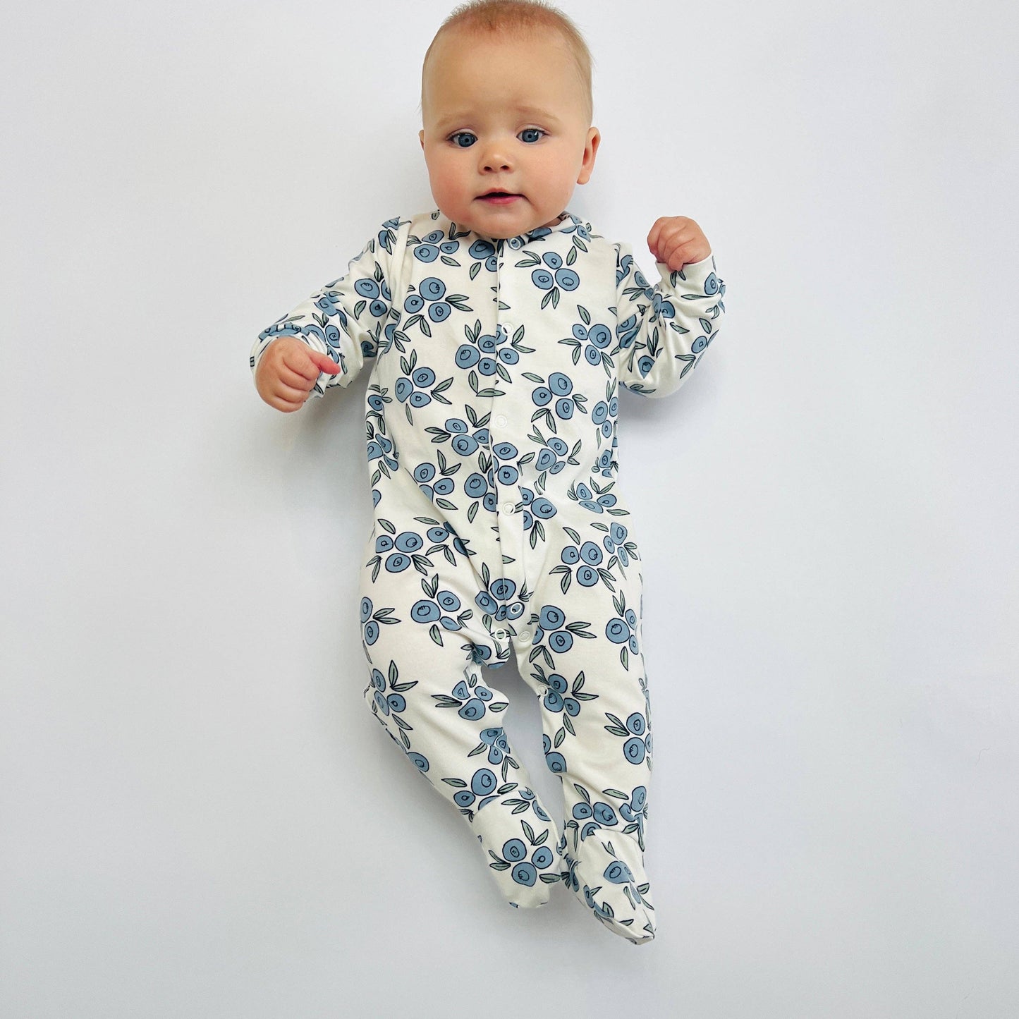 Baby wearing a floral sleepsuit on a plain background