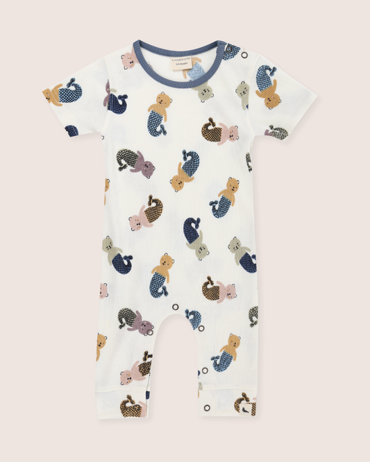 Baby wearing a romper with animal prints sitting on a white surface.