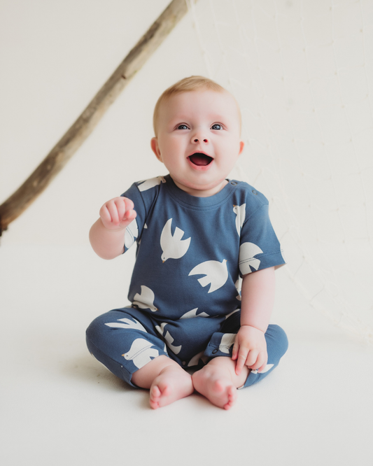 Baby wearing a blue outfit with white bird patterns on a light background