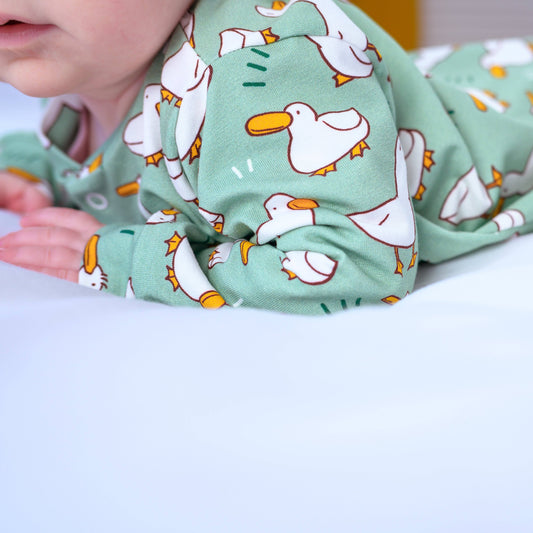 Baby wearing a green sleepsuit with animal patterns on a white background