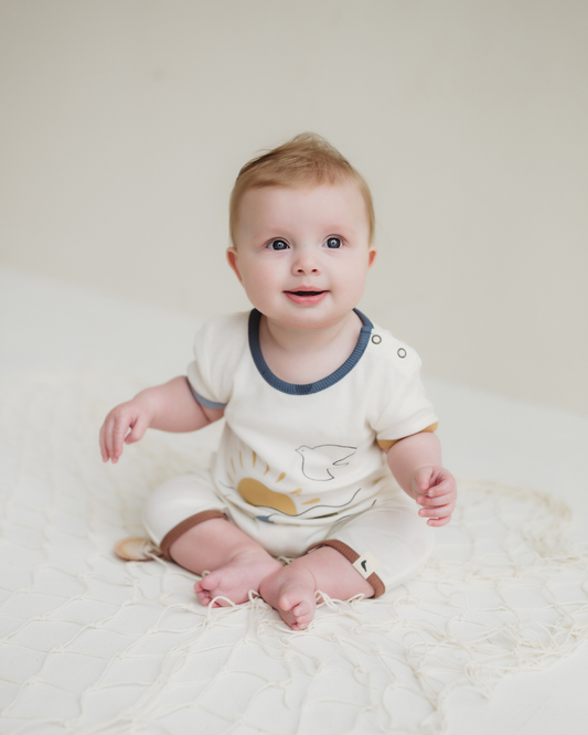 Baby wearing a white romper with animal prints on a light background