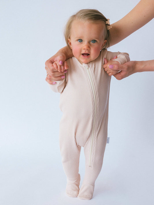Child wearing a beige ribbed romper with a plain background