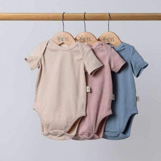 Three baby bodysuits in beige, pink, and blue hanging on a rack with 'Nenby' branding.