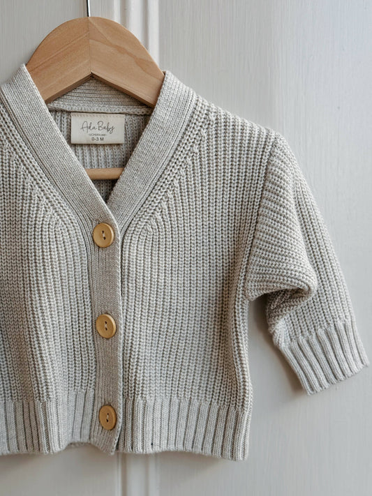 Baby cardigan with buttons on a wooden hanger against a white paneled wall
