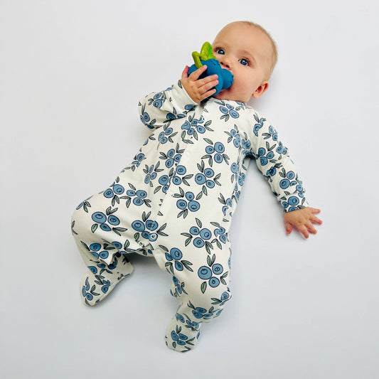 Baby wearing a floral sleepsuit holding a blue toy on a light gray background
