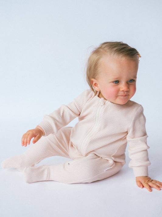 Child wearing a beige ribbed romper with a plain background