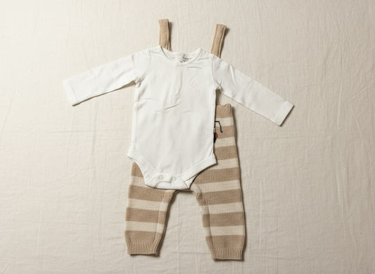 Striped baby dungaree with toy truck pattern on a beige surface