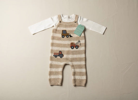 Striped baby dungaree with toy truck pattern on a beige surface