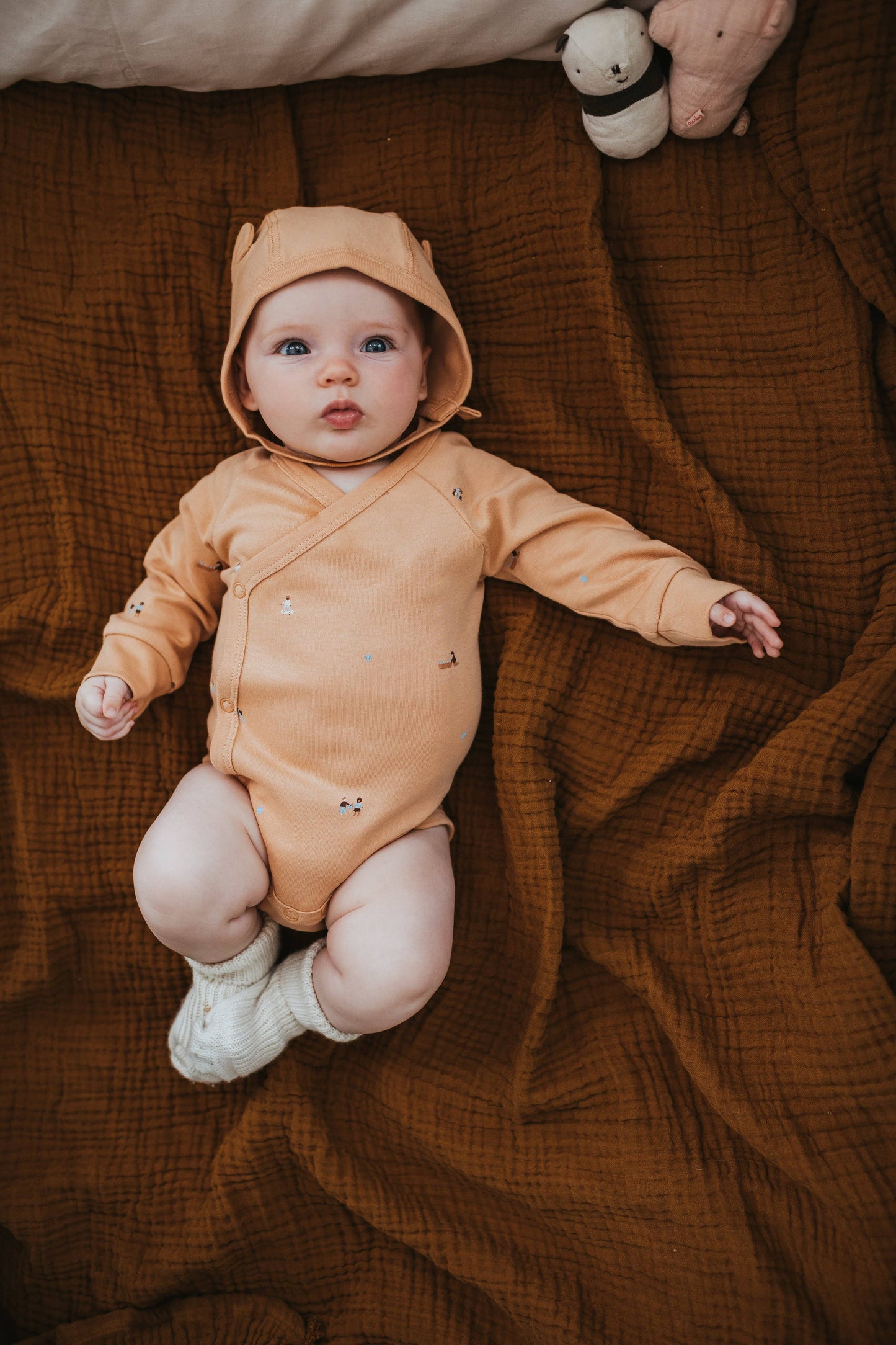 Baby in a mustard yellow onesie lying on a brown textured blanket