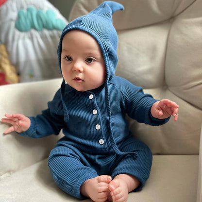 Baby wearing a blue knitted outfit sitting on a beige couch.