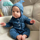 Baby wearing a blue knitted outfit sitting on a beige couch.