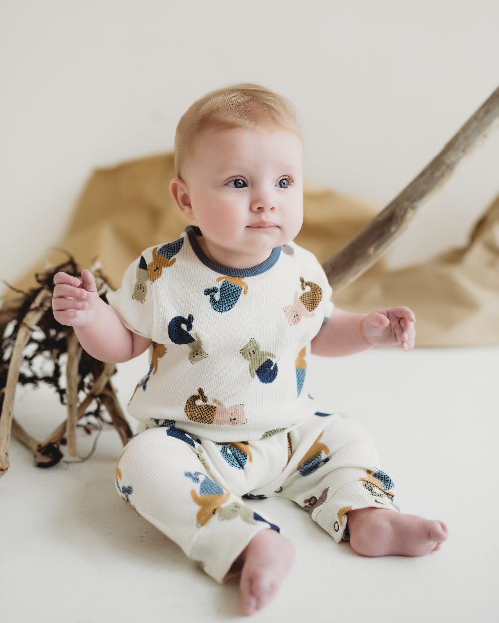 Baby wearing a romper with animal prints sitting on a white surface.