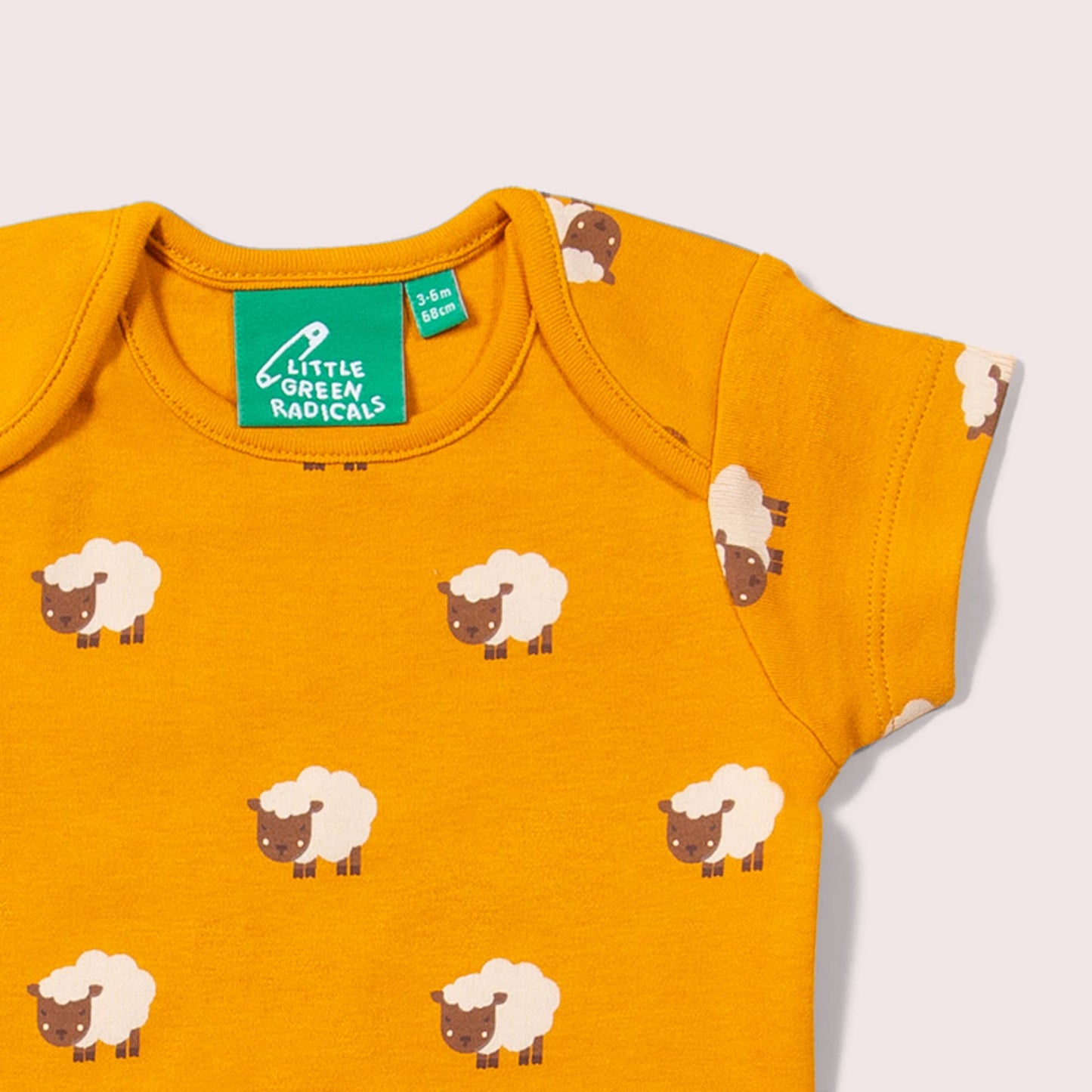 Yellow baby bodysuit with sheep pattern and Green Radicals label on a light gray background