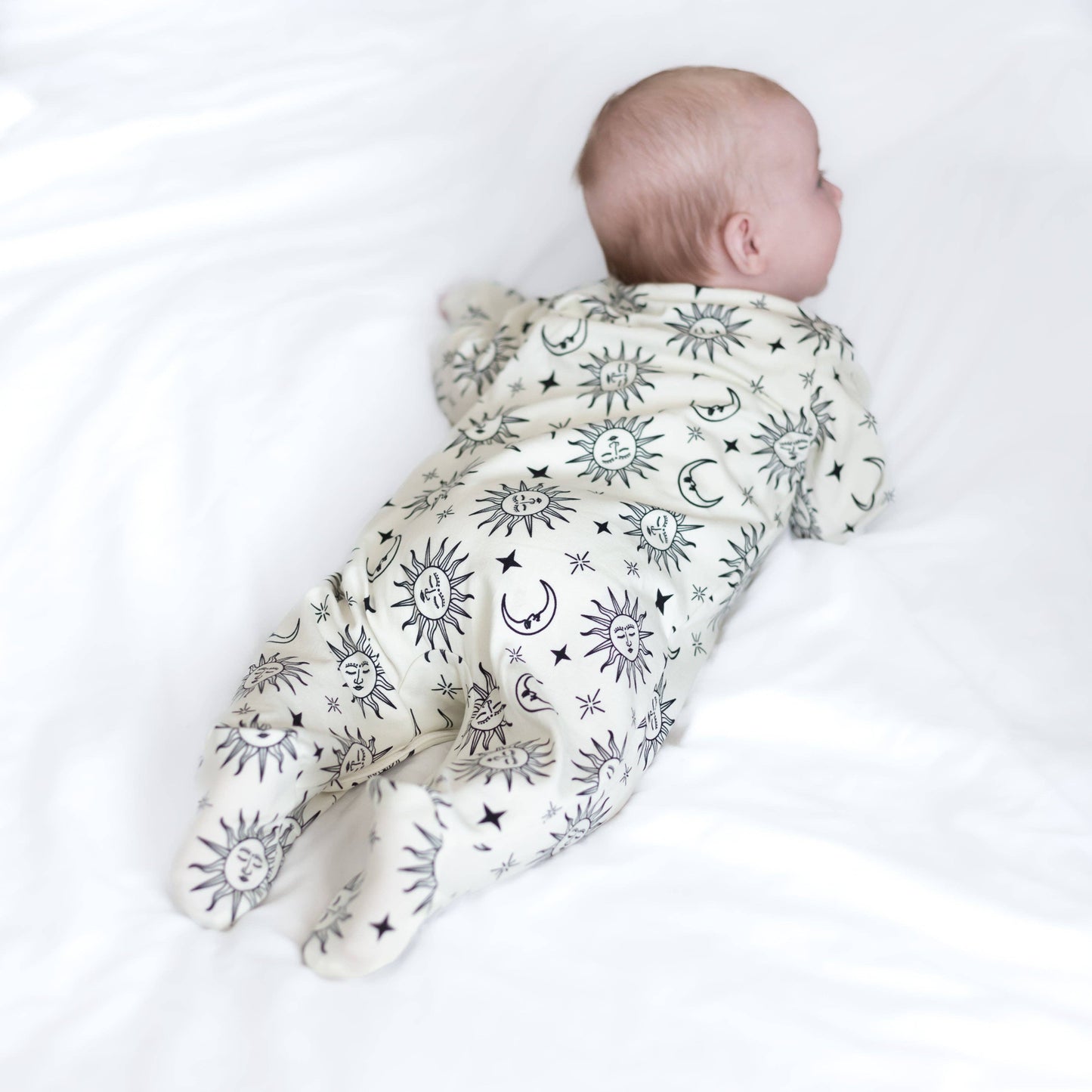 Baby wearing a white sleepsuit with celestial pattern on a white background