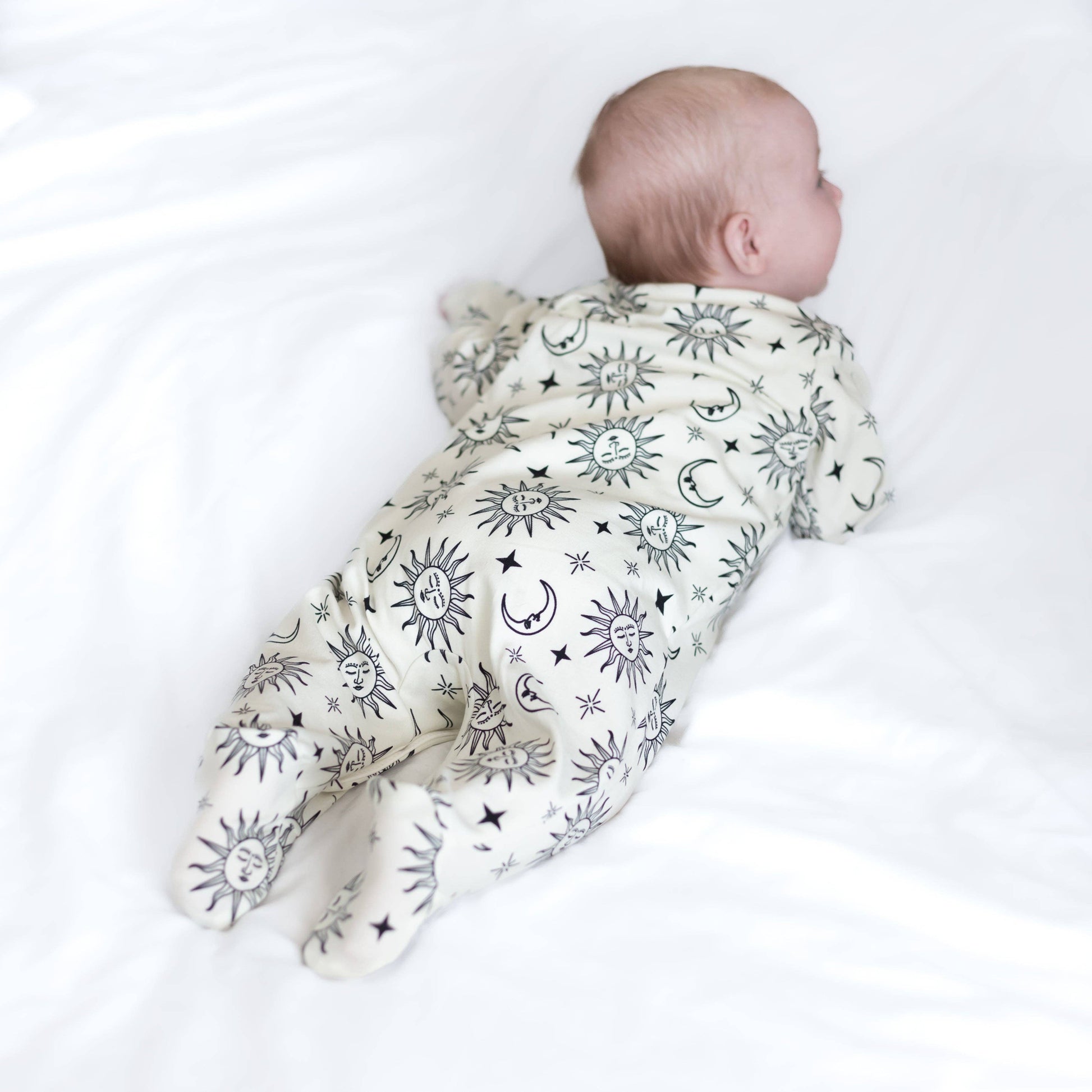 Baby wearing a white sleepsuit with celestial pattern on a white background