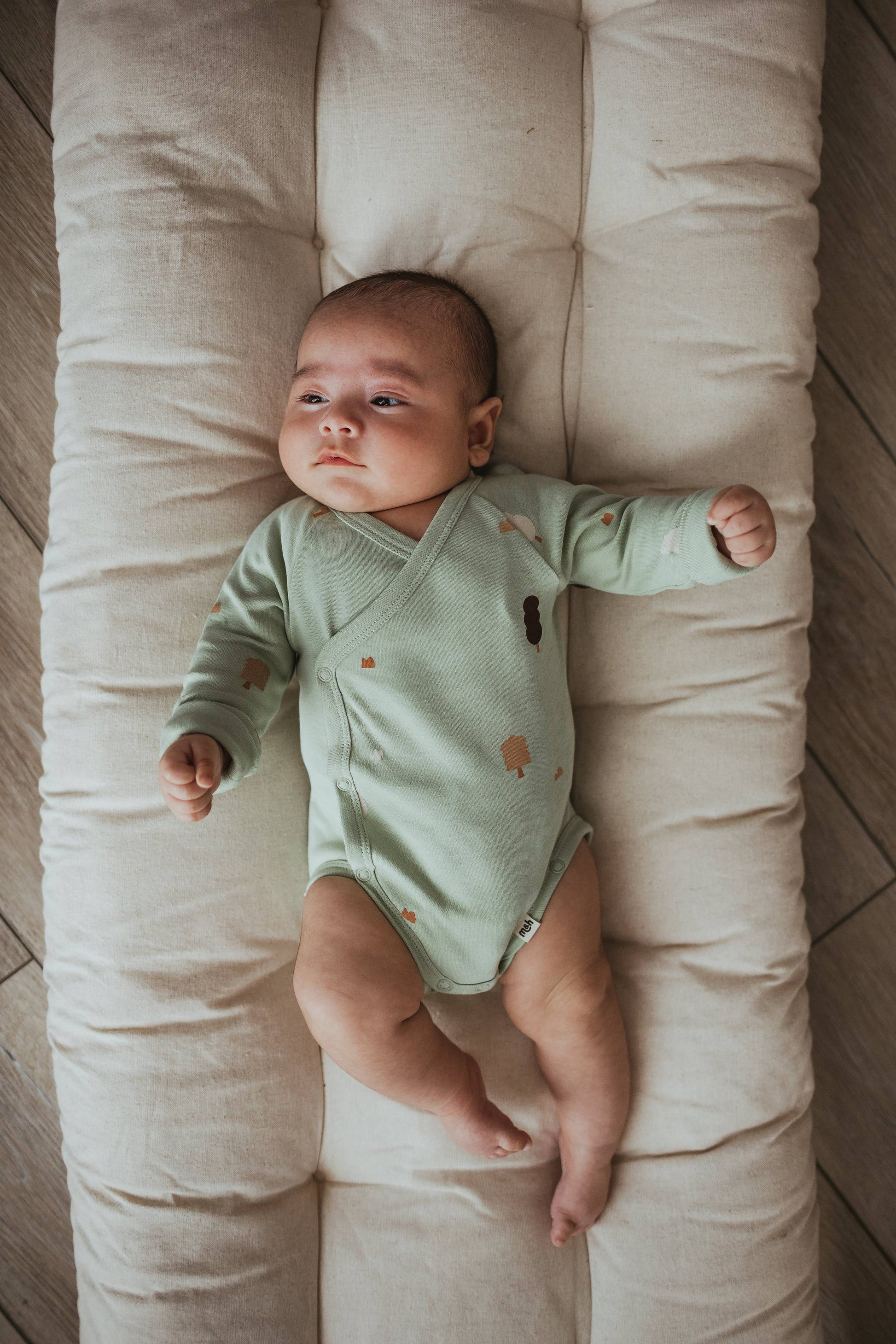 Baby in a green onesie lying on a cushioned surface