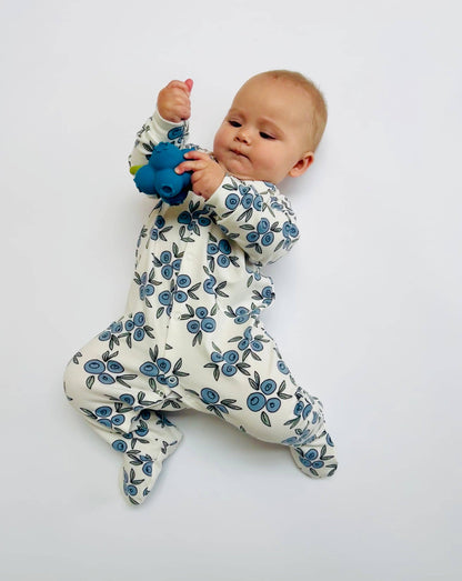 Baby in a floral sleepsuit holding a blue toy on a white background