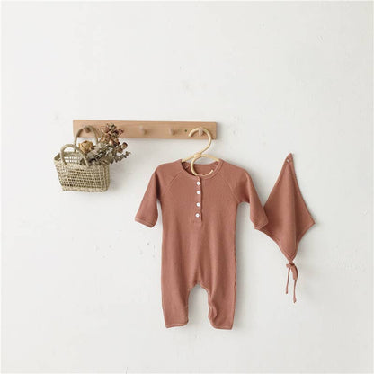 Brown baby romper with a matching blanket on a white wall with a wooden hook.