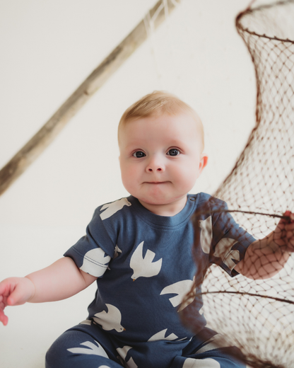 Baby wearing a blue onesie with bird patterns, sitting next to a fishing net.