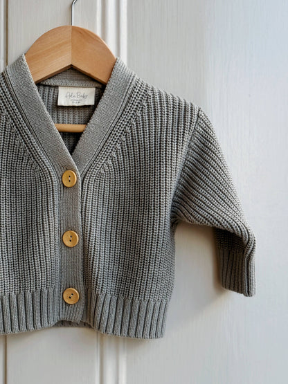 Gray knitted cardigan with wooden buttons on a hanger against a white background