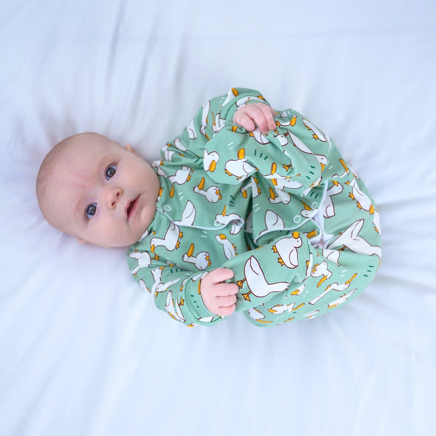 Baby wearing a green sleepsuit with duck pattern on a white background