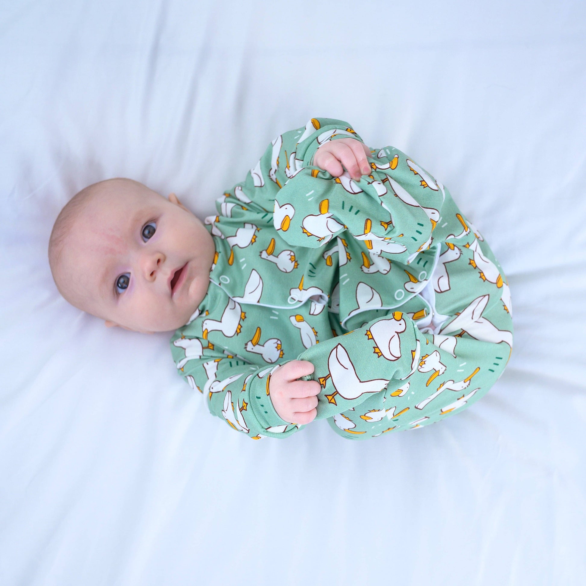 Baby wearing a green sleepsuit with duck pattern on a white background