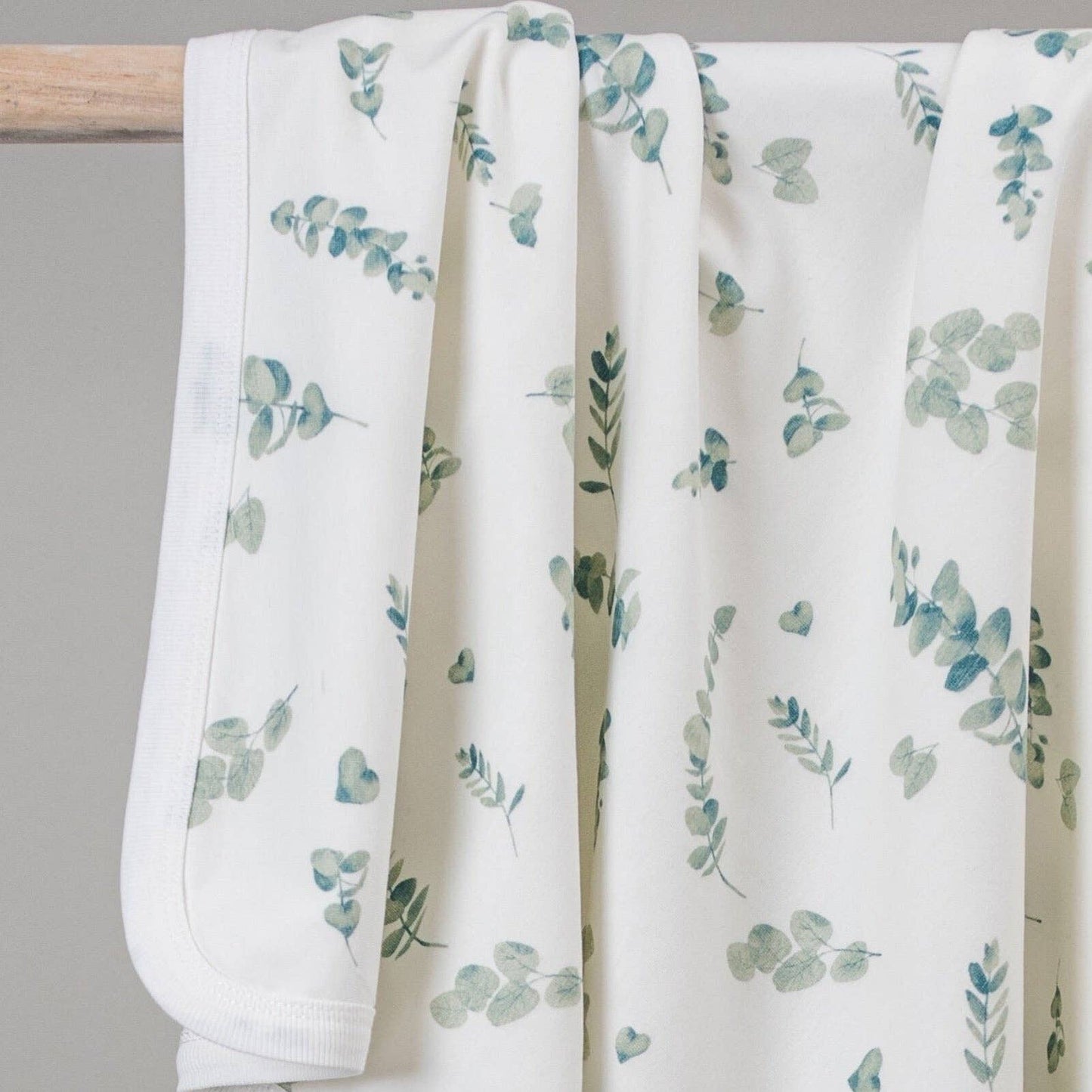 White fabric with green leaf pattern draped over a wooden rod against a gray background