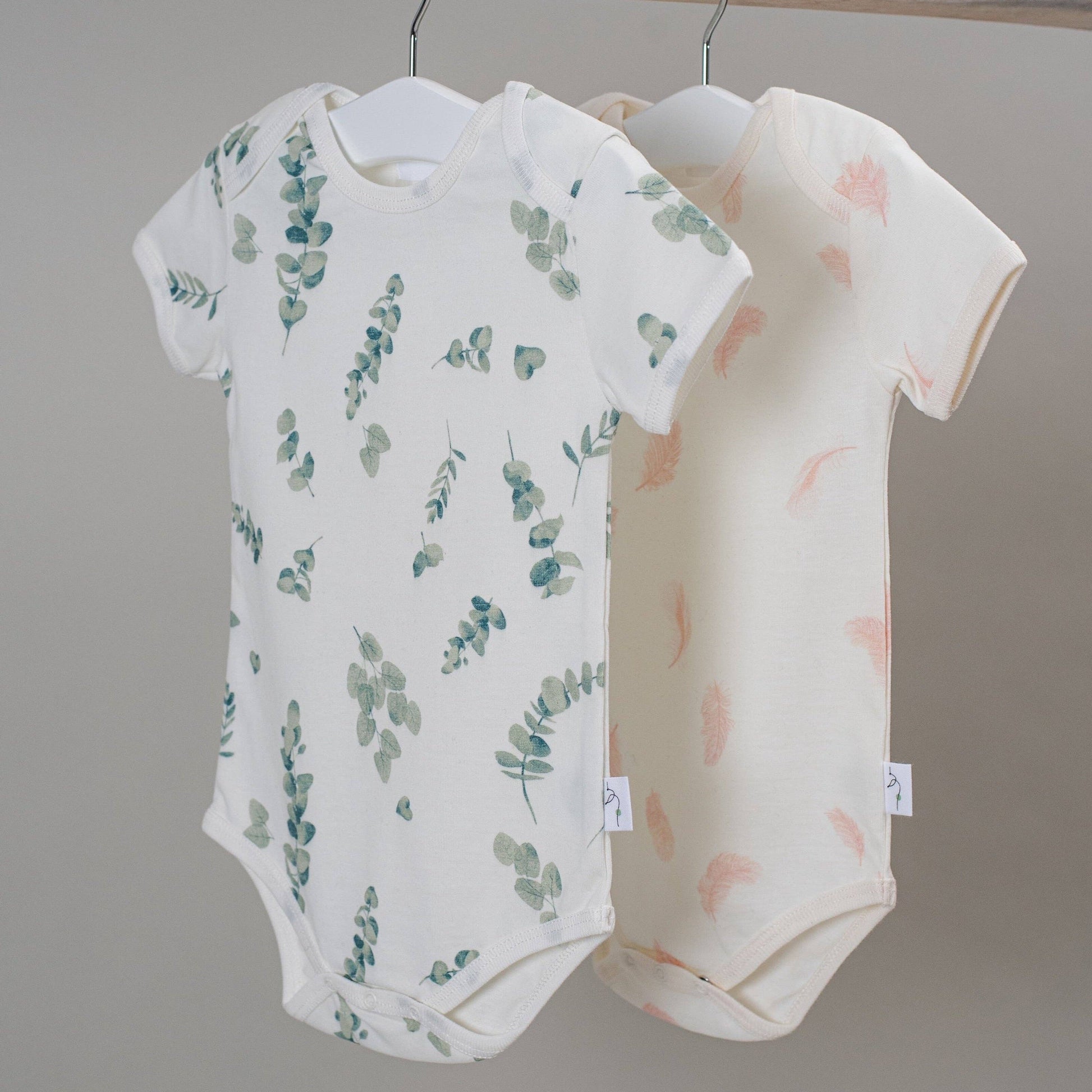 Two baby bodysuits with floral patterns hanging against a neutral background