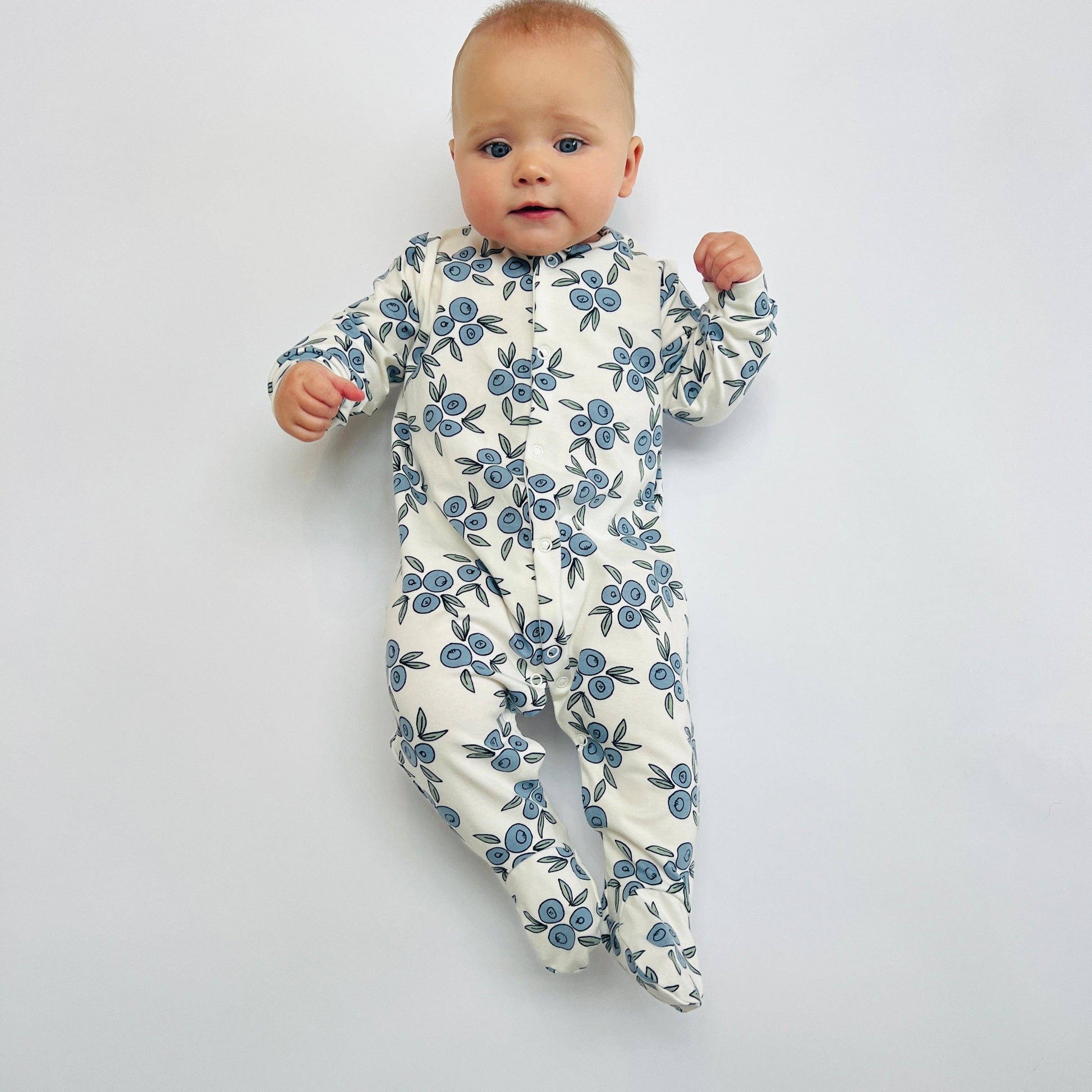 Baby wearing a floral sleepsuit on a plain background