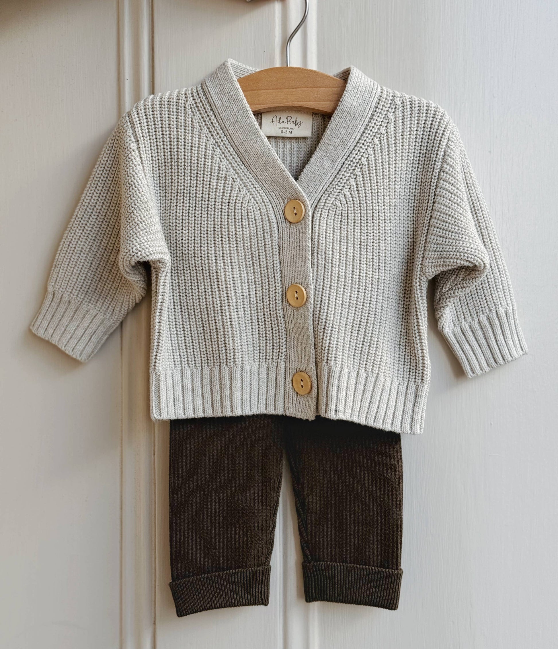 Children's gray knit cardigan with button details and brown pants on a hanger against a white background.