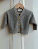 Gray knitted cardigan with gold buttons on a wooden hanger against a white paneled wall.
