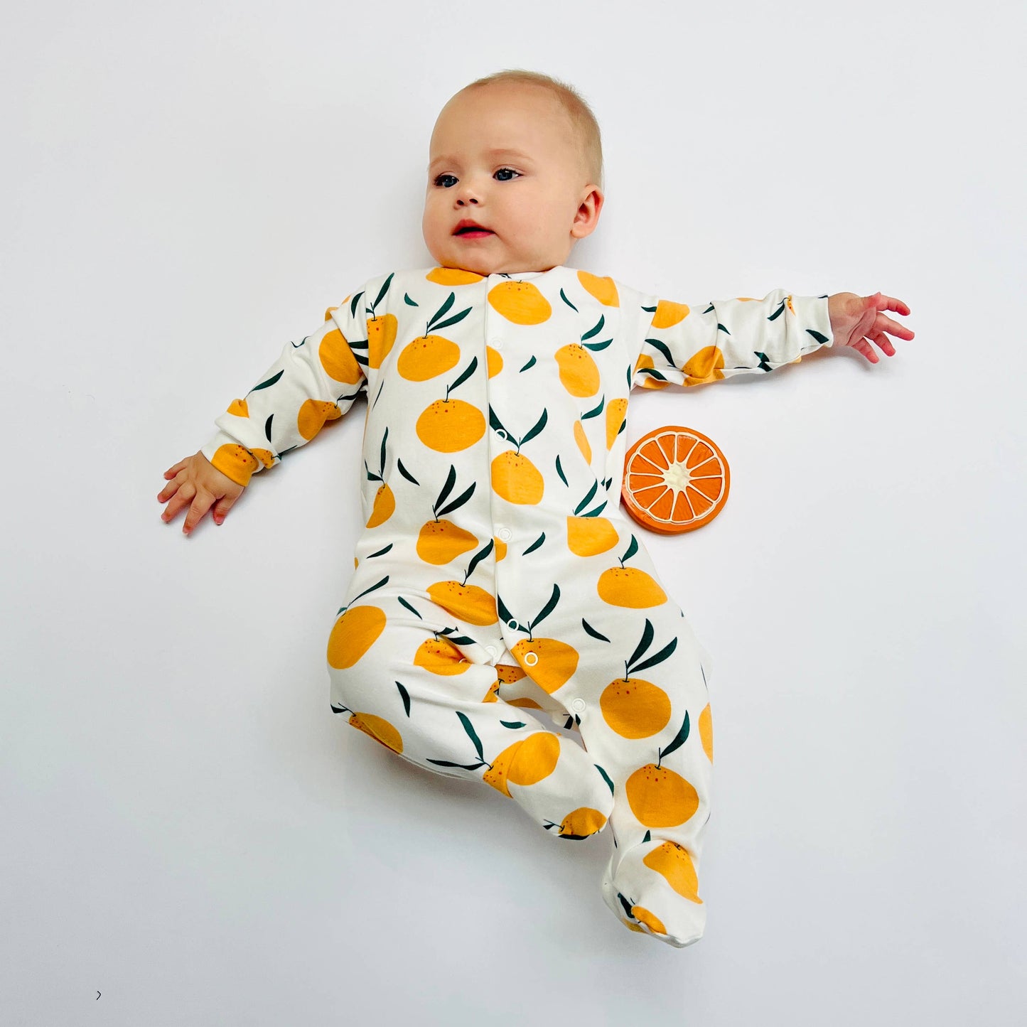 Baby wearing a sleepsuit with orange pattern on a white background