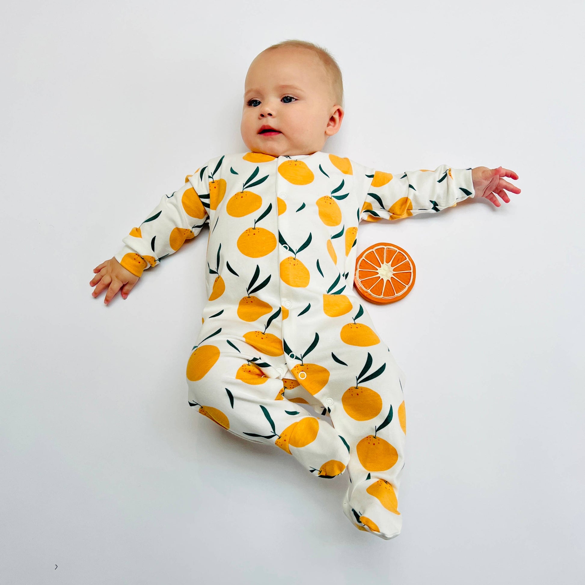 Baby wearing a sleepsuit with orange pattern on a white background