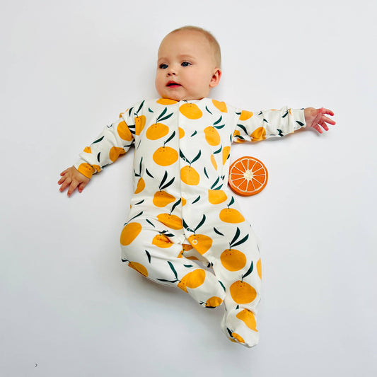 Baby wearing a sleepsuit with orange pattern on a white background