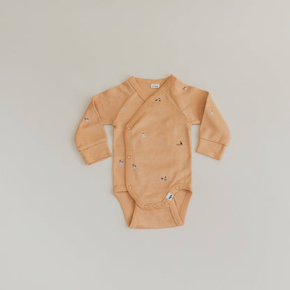Beige baby onesie with small patterns on a light gray background