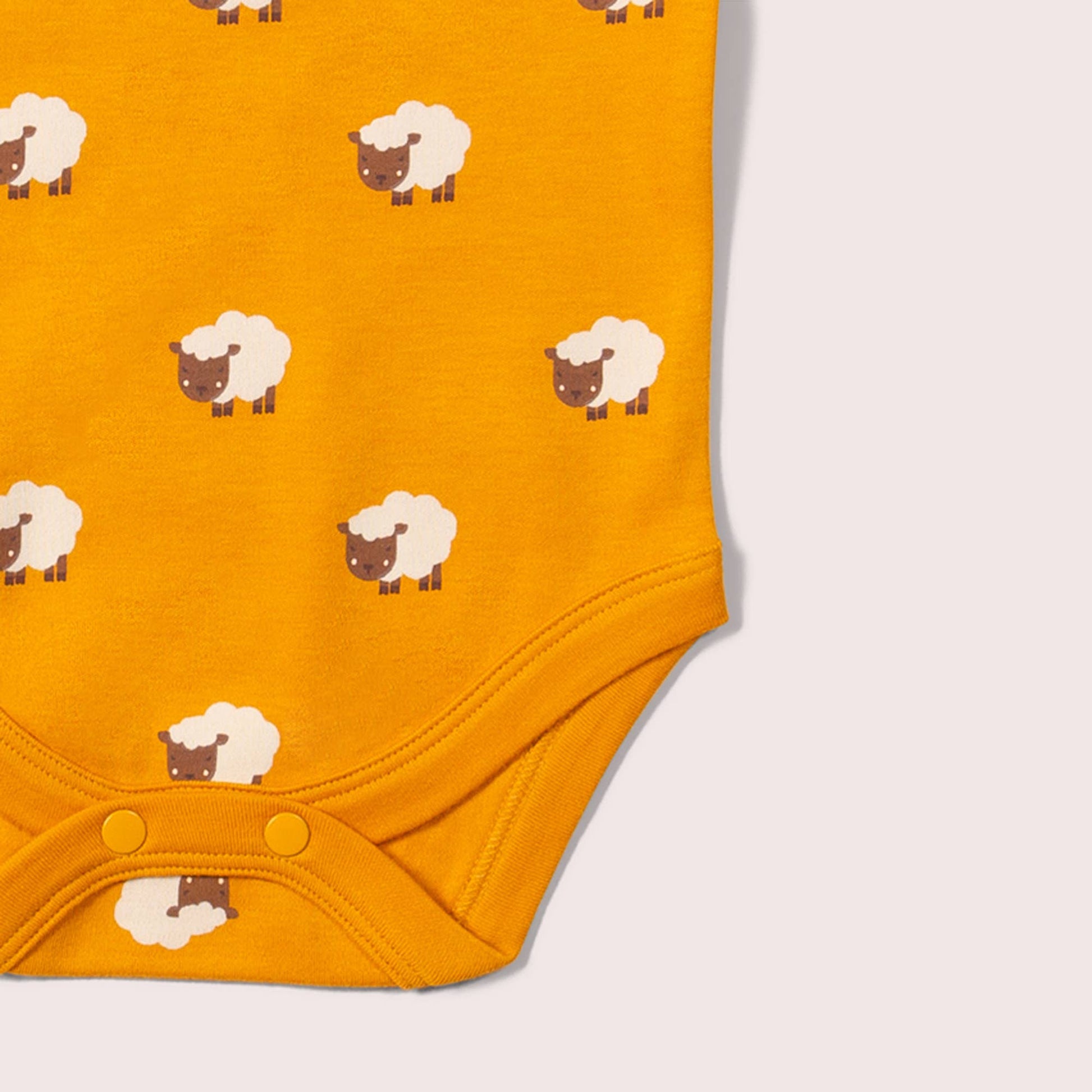 Yellow baby bodysuit with sheep pattern on a light gray background