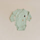 Mint green baby onesie with tree designs on a beige background