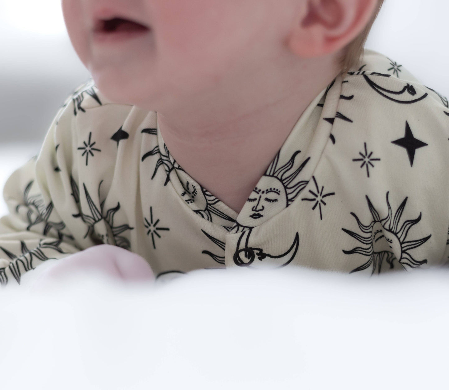 Close-up of a baby wearing a patterned sleepsuit with black designs on a neutral background