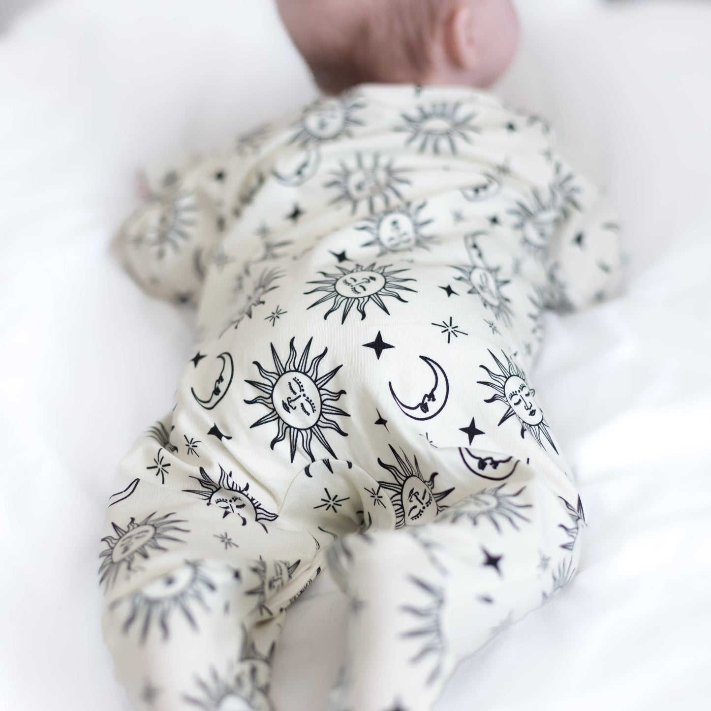 White baby sleepsuit with black celestial pattern held by a hand on a white background