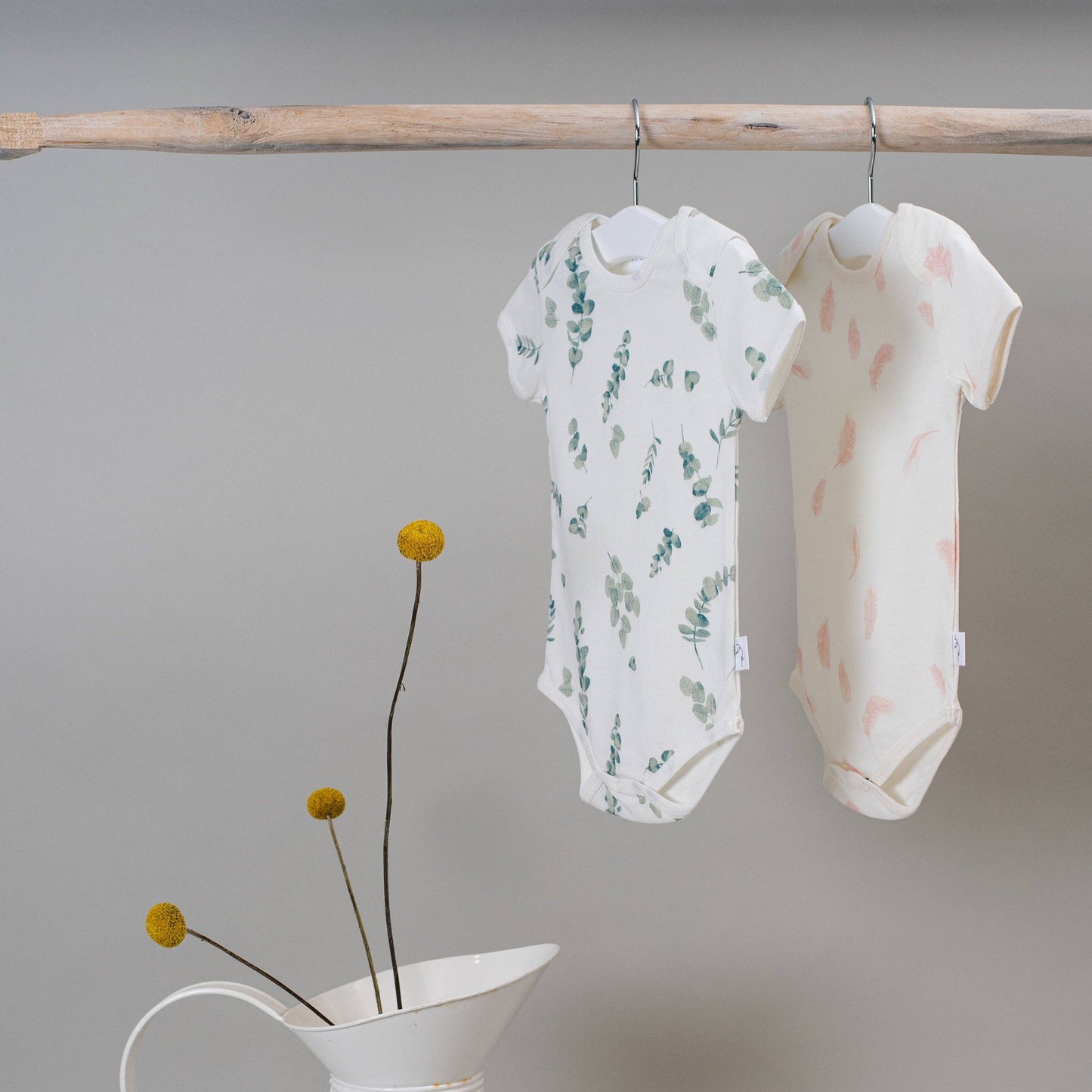 Two baby rompers hanging on a wooden rod with a minimalistic background.