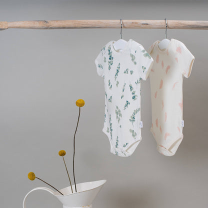 Two baby rompers hanging on a wooden rod with a minimalistic background.